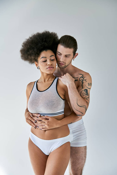 όμορφη νεαρή Αφροαμερικανή γυναίκα και το αγόρι της με τα τατουάζ αγκαλιάζονται θερμά, σέξι ζευγάρι - Φωτογραφία, εικόνα