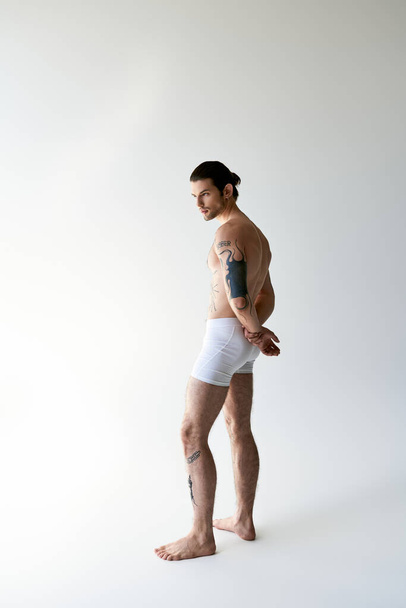 sexy sterke man met paardenstaart en koele tatoeages poseren in comfortabele ondergoed op ecru achtergrond - Foto, afbeelding