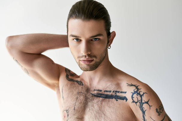 jonge knappe man met paardenstaart en koele tatoeages in comfortabele ondergoed poseren op ecru achtergrond - Foto, afbeelding
