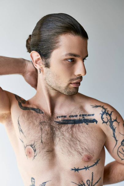 sexy good looking man with ponytail and tattoos in comfy underwear posing on ecru background - Фото, изображение