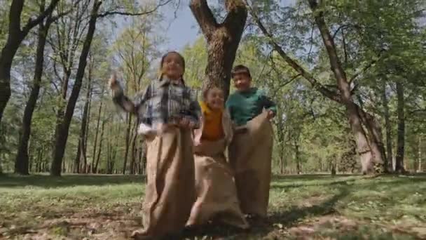 Повний знімок грайливих маленьких дітей, які стрибають мішками і розважаються в парку в літній день - Кадри, відео
