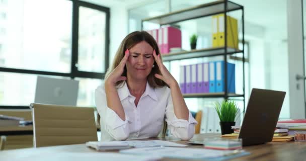 Trabalhadora de escritório mulher perturbada toca cabeça sofrendo de dor de cabeça à mesa com documentos e laptop. Sobrecarga de trabalho e problemas de saúde física - Filmagem, Vídeo