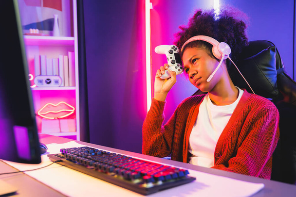 Afro-Amerikaanse meisje streamer teleurgesteld spelen online vechten met Esport ervaren team het dragen van een koptelefoon in neon kamer. Praten met andere spelers planing strategieën om concurrenten te winnen. Smaakstof. - Foto, afbeelding