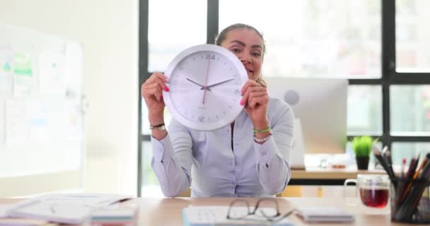 Employée heureuse entreprise tient horloge murale indiquant la fin de la journée de travail. Concept de temps et d'émotions positives au bureau au ralenti - Séquence, vidéo