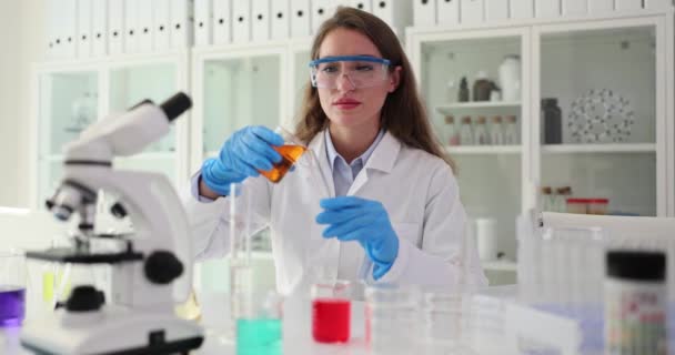 Γυναίκα χημικός χύνει υγρό από γυάλινο δοχείο σε σωλήνα κάθεται στο τραπέζι με μικροσκόπιο και επαγγελματικό εξοπλισμό για ιατρική έρευνα. Ροές εργασίας εμπειρογνωμόνων - Πλάνα, βίντεο