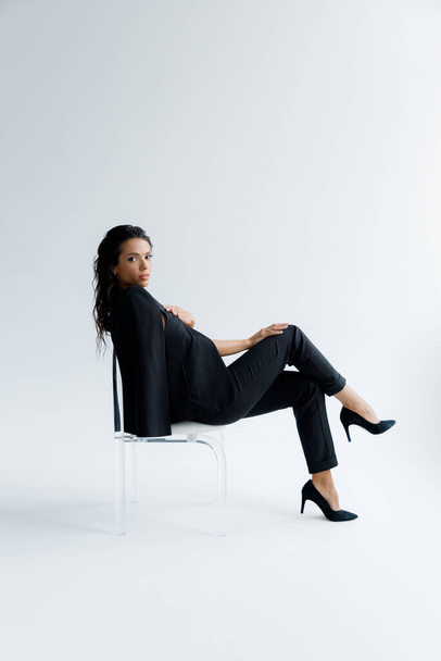 Une fille sexy et belle de luxe lors d'une séance photo dans un studio photo pose élégamment et à la mode dans un costume de pantalon noir - Photo, image