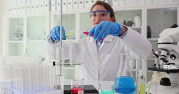 Empleada profesional del laboratorio mezcla muestras en un recipiente de vidrio realizando un experimento. Mezcla de líquidos de diferentes colores en cámara lenta - Metraje, vídeo
