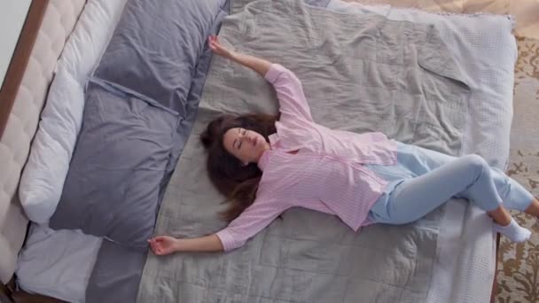 A young harried woman in the bedroom falls, spreads hands and lie on the bed tiredly after cleaning housework or coming from work. A lady is exhausted, puts hand on her forehead, yawns, wants to sleep - Footage, Video