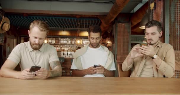Ryhmä kiireinen miesten ystäviä istuu pubissa ja kaikki käyttävät älypuhelinta, tarkkailun sanansaattaja tai vieritys sosiaalisen median. Kännykkäriippuvuus. Vakavia miehiä katsomassa matkapuhelimissa  - Materiaali, video