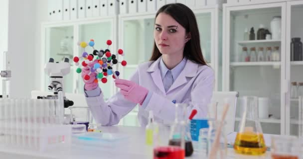 La chimica femminile focalizzata punta penna a modello molecolare in mano. Insegnante donna in camice spiega la struttura della materia in laboratorio scientifico slow motion - Filmati, video