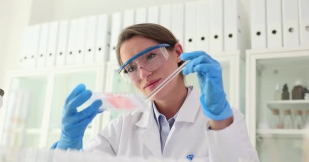 Woman worker in field of research examines specimen in glass sitting at workplace in office. Chemist makes discovery in laboratory slow motion - Footage, Video