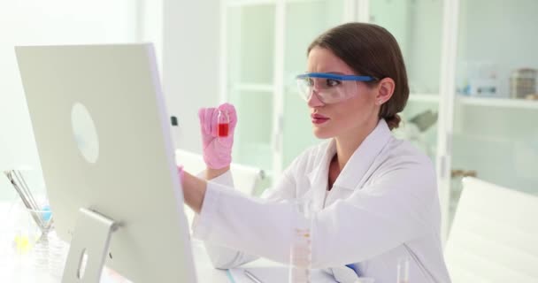 Química femenina que busca el nombre de la muestra en la base de datos de la computadora que contiene líquido en un vaso pequeño en el laboratorio. Flujo de trabajo profesional cámara lenta - Imágenes, Vídeo