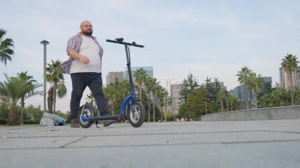 Homme en surpoids équitation scooter électrique dans la ville. Homme conduisant e-scooter à l'extérieur. Transport électrique et écologique. Transport respectueux de l'environnement. Concept de mode de vie durable. - Séquence, vidéo