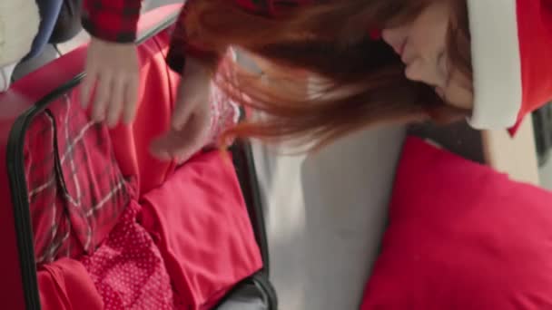Жінка в капелюсі Діда Мороза упаковує речі у валізу, щоб поїхати на зимові канікули. В очікуванні новорічної подорожі. Підготовка до різдвяної подорожі. У червоних кольорах. Високоякісні 4k кадри - Кадри, відео