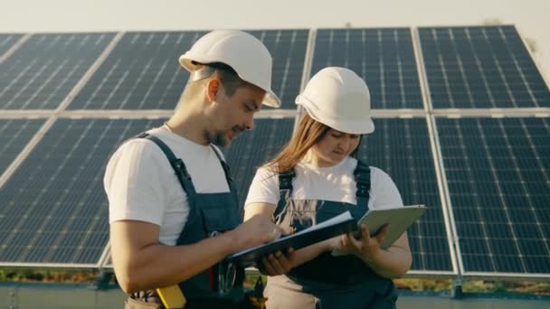 Az alternatív villamos energia előállításához használt overallokban dolgozó munkavállalók adatokat gyűjtenek és elemeznek.Energiatermelés napelemekkel, zöld energiával.Egy mezőn elhelyezett ökológiai erőmű napelemei - Felvétel, videó
