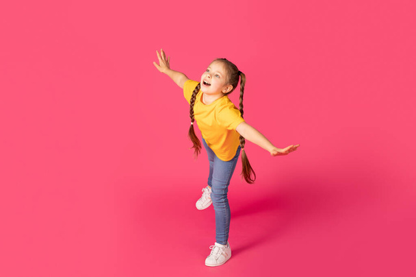 Веселые Preteen Кавказская девушка дурачится на розовом фоне, счастливый ребенок-подросток в повседневной одежде, разбрасывая руки и притворяясь летая, веселясь в студии, полный снимок длины, скопировать пространство - Фото, изображение