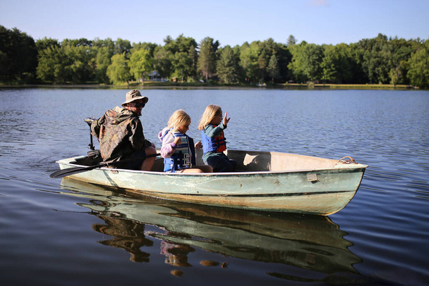 Niña niños con chalecos salvavidas están montando en un pequeño barco de pesca de aluminio con un motor de curricán con su padre en un lago. - Foto, Imagen