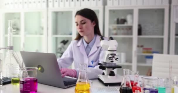 Chimica donna concentrata guarda campione al microscopio in clinica. Impianto medico per prove con apparecchiature per condurre esperimenti al rallentatore - Filmati, video