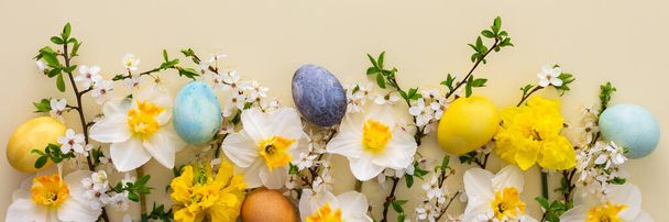 Banner festivo con flores de primavera y huevos de Pascua, narcisos blancos y ramas de flor de cerezo sobre un fondo amarillo pastel - Foto, Imagen