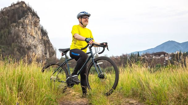黄色い服を着た髭の男のサイクリストが自然の中で自転車に乗って休んでいます。健康のためのスポーツ趣味娯楽 - 写真・画像