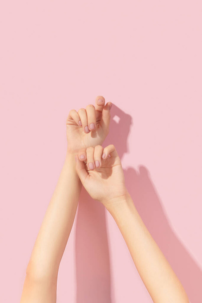 Mooie geprepareerde vrouwen handen met roze matte nagel ontwerp op een roze achtergrond. Manicure, pedicure schoonheidssalon. Lege plaats voor tekst - Foto, afbeelding