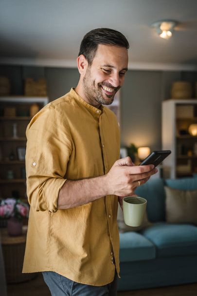 jeden mężczyzna dorosły biały mężczyzna używać telefon komórkowy smartfon do wysyłania wiadomości SMS lub przeglądać internet podczas stać w domu nosić koszulę i okulary prawdziwa osoba skopiować przestrzeń szczęśliwy uśmiech - Zdjęcie, obraz