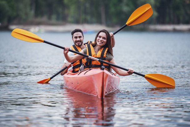 Happy young couple in sea vests is smiling while sailing a kayak - Photo, Image