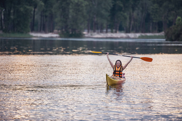 Красивая молодая женщина в жилете улыбается во время плавания на каяке
 - Фото, изображение