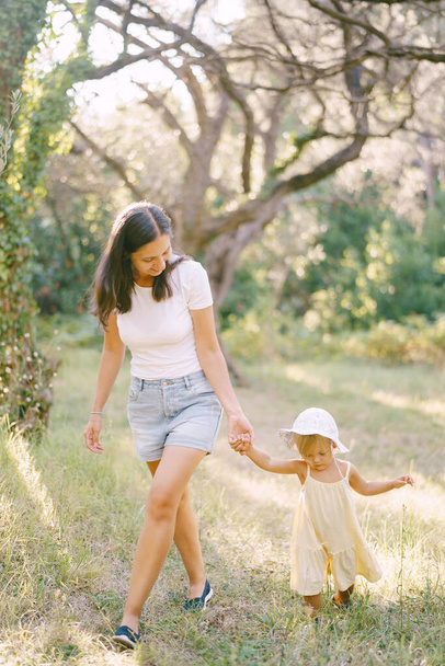 ママは緑の公園を通って小さな女の子を手で導き,足を見つめている. 高品質の写真 - 写真・画像