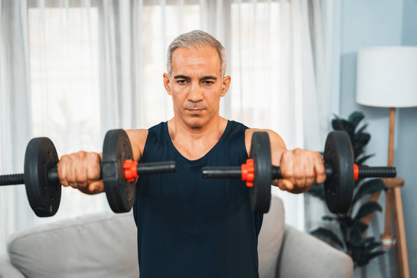 Urheilullinen ja urheilullinen vanhempi mies harjoittaa kehon harjoitus rutiini nostamalla käsipaino kotona käsitteenä terveen istuvuuden kehon paino elämäntapa eläkkeelle siirtymisen jälkeen. Vaikutusvalta - Valokuva, kuva