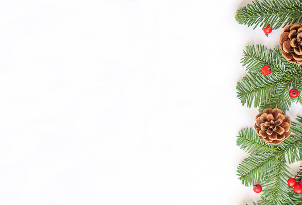 Рождественская плоская композиция. Зеленые ветки с красными ягодами и коричневыми шишками на белом фоне. Высокое качество фото - Фото, изображение