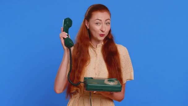 Hey you, call me back. Adult woman talking on wired vintage telephone of 80s, says hey you call me back, conversation proposition, hot line. Redhead girl isolated on blue studio background indoors - Footage, Video