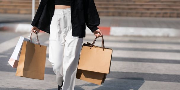 Молодая азиатка в магазине. Модная женщина в черном с сумкой для покупок гуляет по городу после покупок. Чёрная пятница. - Фото, изображение