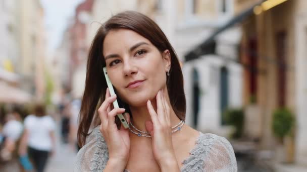 Happy pretty woman having remote conversation communicate speaking by smartphone. Handsome young adult girl talking on phone unexpected good news gossip walking in city street. Town lifestyles outdoor - Footage, Video