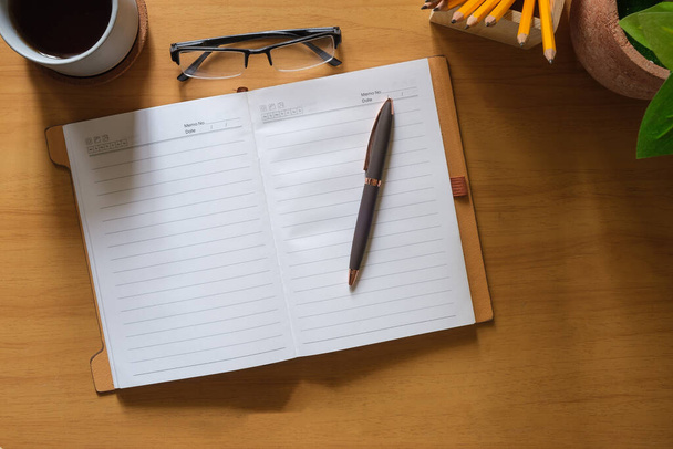 Otwórz notatnik, długopis, szklanki i filiżankę kawy na drewnianym biurku. Widok z góry z miejsca na tekst. - Zdjęcie, obraz
