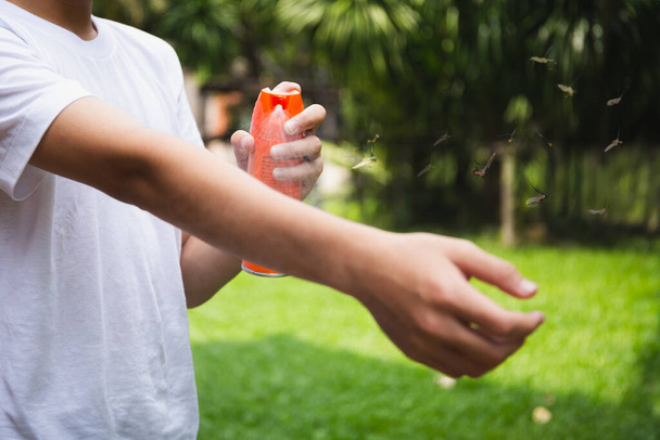 Young boy spraying insect repellents on skin in the garden with mosquito flying - Photo, Image
