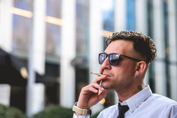 Městský obchodní styl: moderní a mladý profesionál s košilí a kravatou kouření marihuany a tabáku joint v obchodní čtvrti - Fotografie, Obrázek