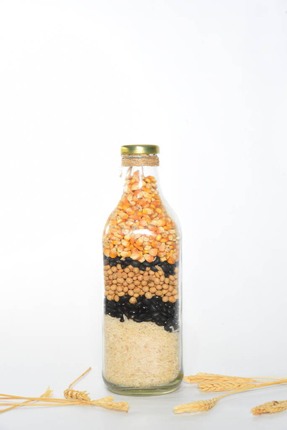 botella de vidrio con granos de cereales arroz, soja, frijoles, maíz sobre fondo blanco
 - Foto, Imagen