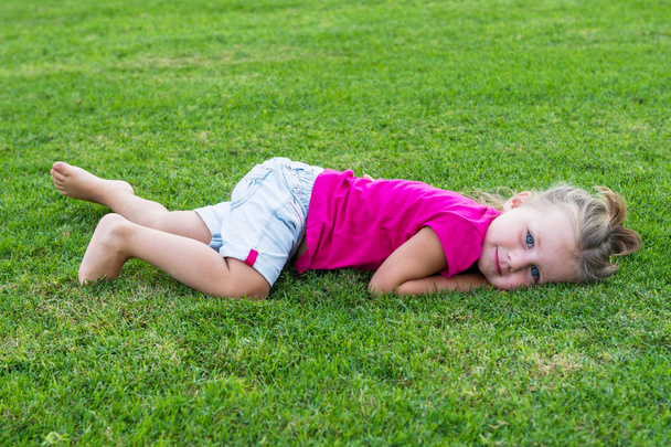 Małe słodkie dziewczyny Europejskiej pozowanie, leżącej w zielonej trawie. - Zdjęcie, obraz