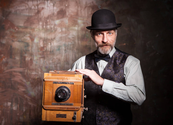 Vaikuttava iäkäs valokuvaaja liivissä ja rusetti vanha puinen kamera - Valokuva, kuva