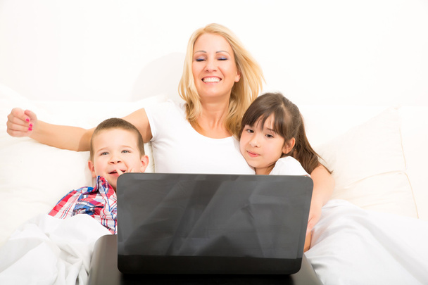 Mother with her kids using a laptop in bed - Foto, imagen