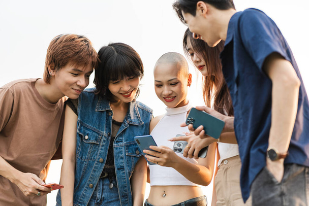 Imagem de um grupo de jovens asiáticos rindo juntos e usando seus telefones - Foto, Imagem