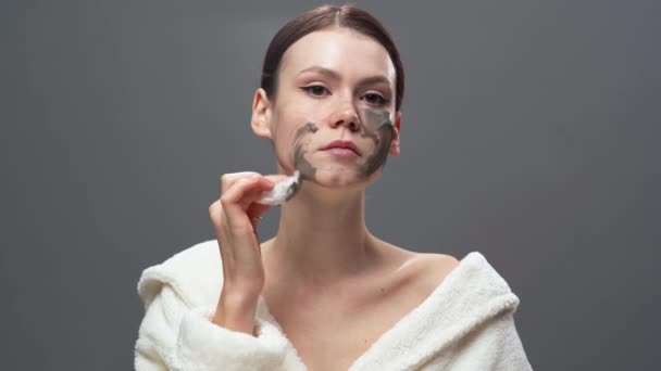 Молода жінка видаляє маску краси для обличчя зі шкіри з серветкою, косметологією та салонним спа-продуктом в студії. Кавказька дівчинка і самодопомога щастя для лицьового сяйва. Копіювати простір - Кадри, відео