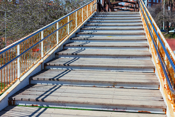 Городской пешеходный мост, оборудованный деревянной лестницей над оживленным шоссе. Деревянная лестница ведет путешественников вверх к центральной аллее моста - Фото, изображение