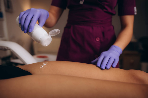 Косметолог поливает тальком женскую ногу перед процедурой депиляции на белом фоне. Высокое качество фото - Фото, изображение