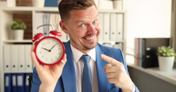 午前10時の赤い目覚まし時計を持つ笑顔のマネージャーの肖像画。勤務日の概念の開始 - 映像、動画