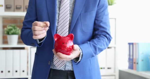 Businessman tosses coins into red piggy bank. Saving savings concept - Footage, Video