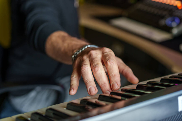 Close-up van de handen van een muzikant die een elektronisch toetsenbord bespeelt met focus op vingers en toetsen, waarbij de essentie van muziekcreatie wordt vastgelegd. - Foto, afbeelding