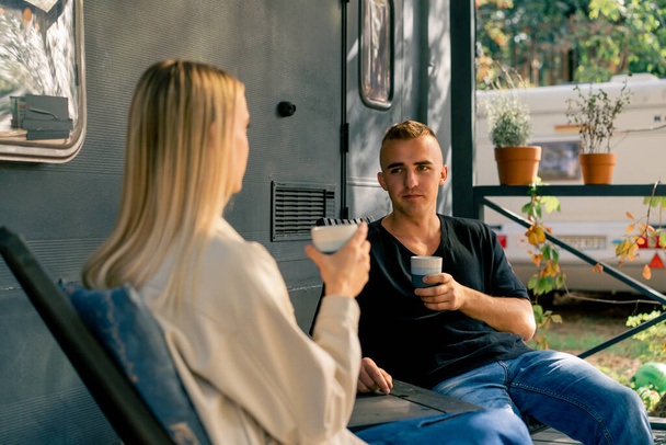 Młody przystojniak i dziewczyna siedzą na werandzie kampera w kamperze pijąc herbatę i entuzjastycznie rozmawiając - Zdjęcie, obraz