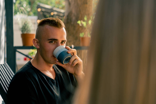 Közelkép egy fiatal fickóról, aki a teraszon ül egy lakókocsi mellett, teát iszik és figyelmesen hallgatja a barátnőjét. - Fotó, kép